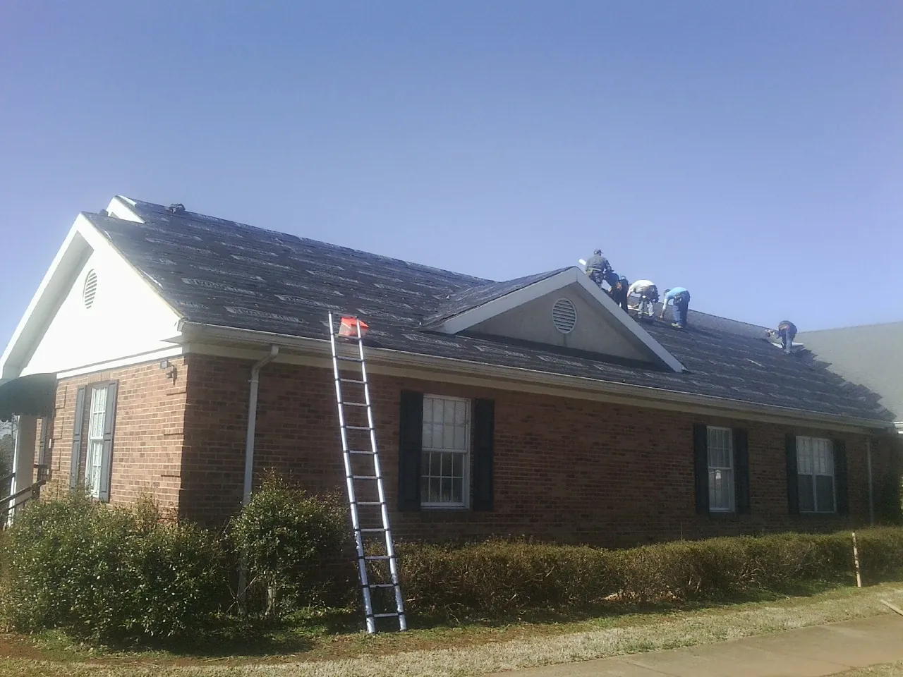 Crew tearing shingles off a brick ranch roof with a ladder set — Emergency Roof Repair work by our crew in Goleta