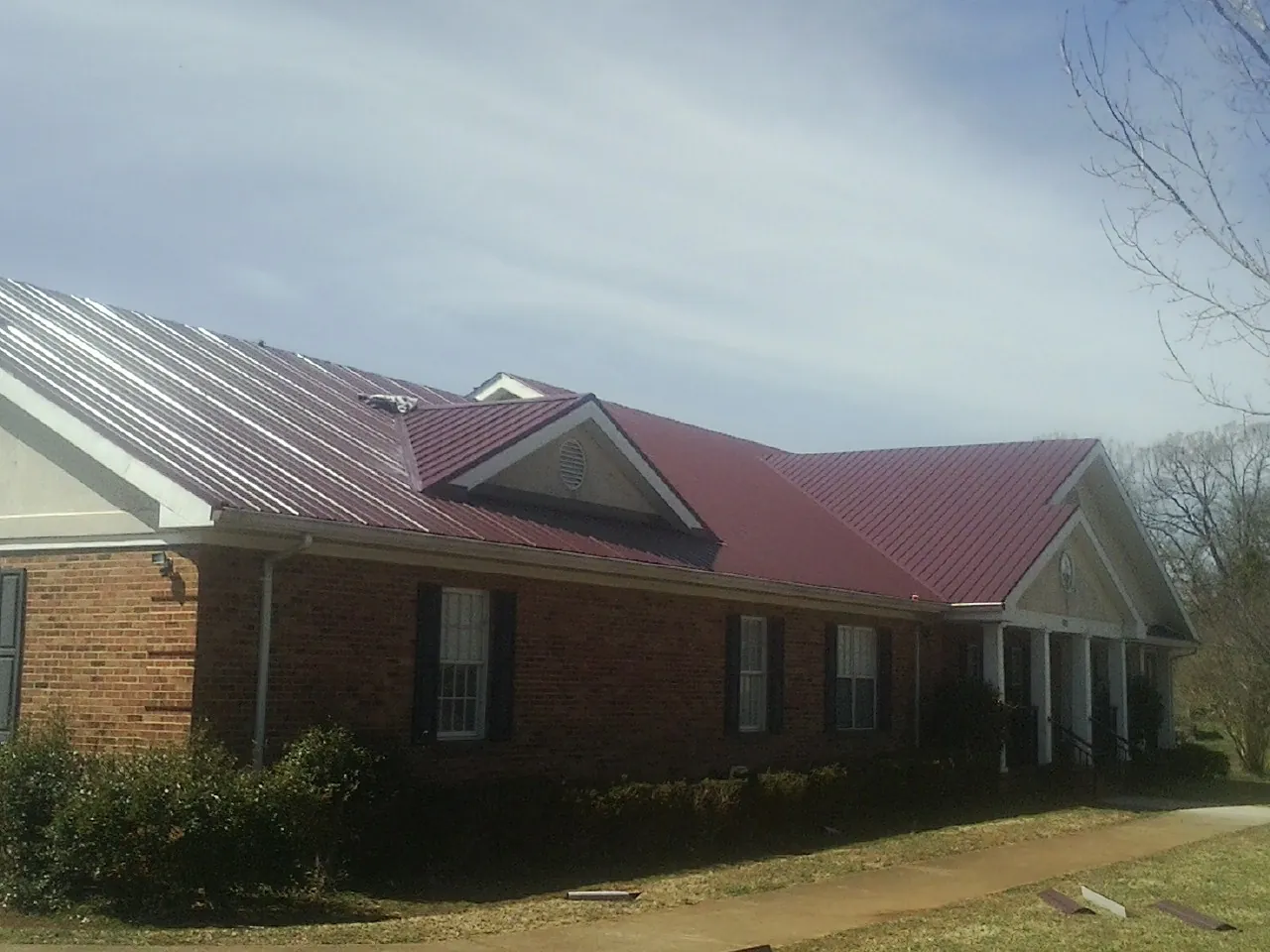 Red metal roof with gabled entries on a long brick building, from a Hail Damage Roof Repair job in Goleta