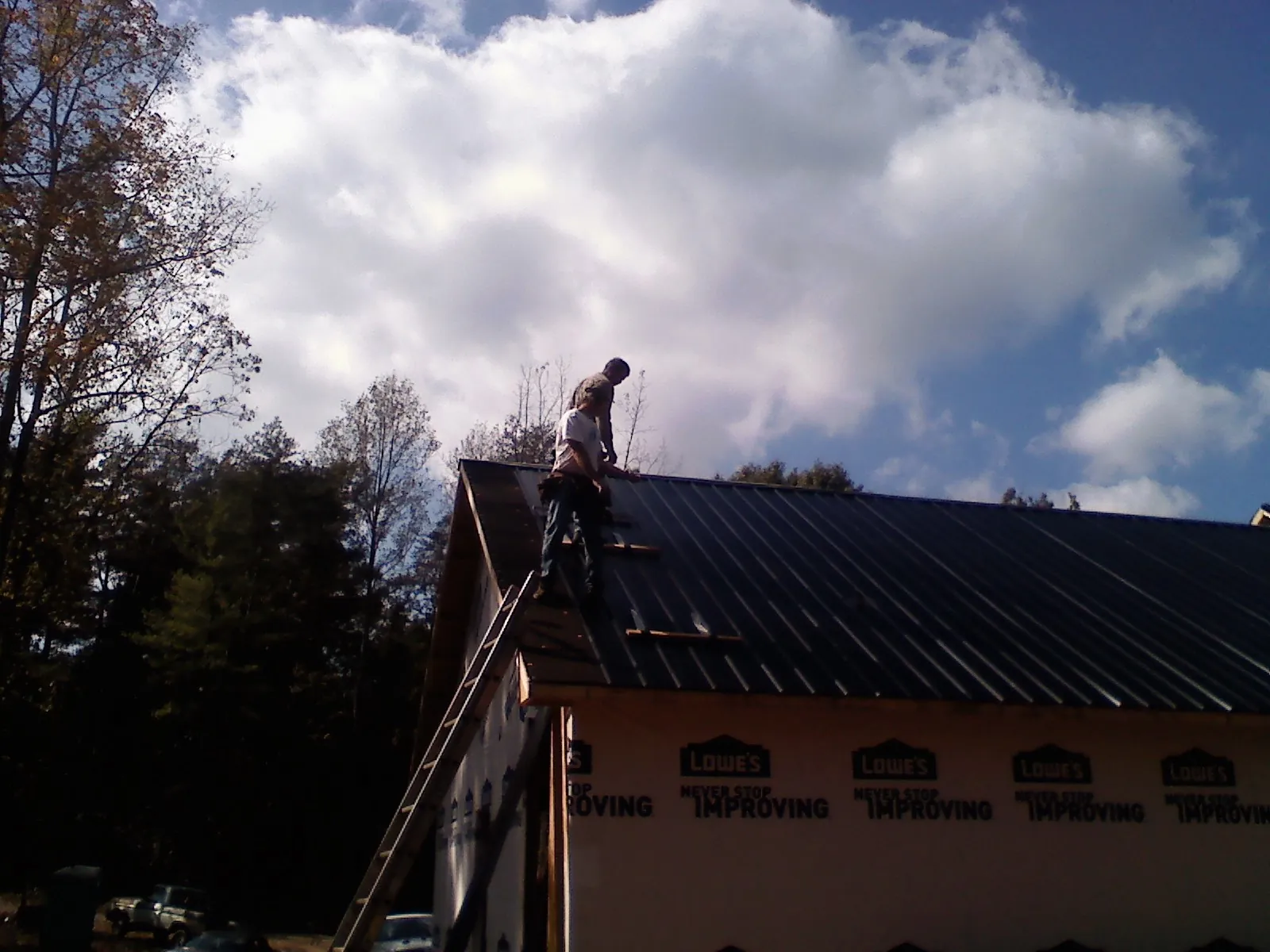 Roofer fastening dark metal panels high against a cloudy sky, from a Roof Inspection job in Goleta