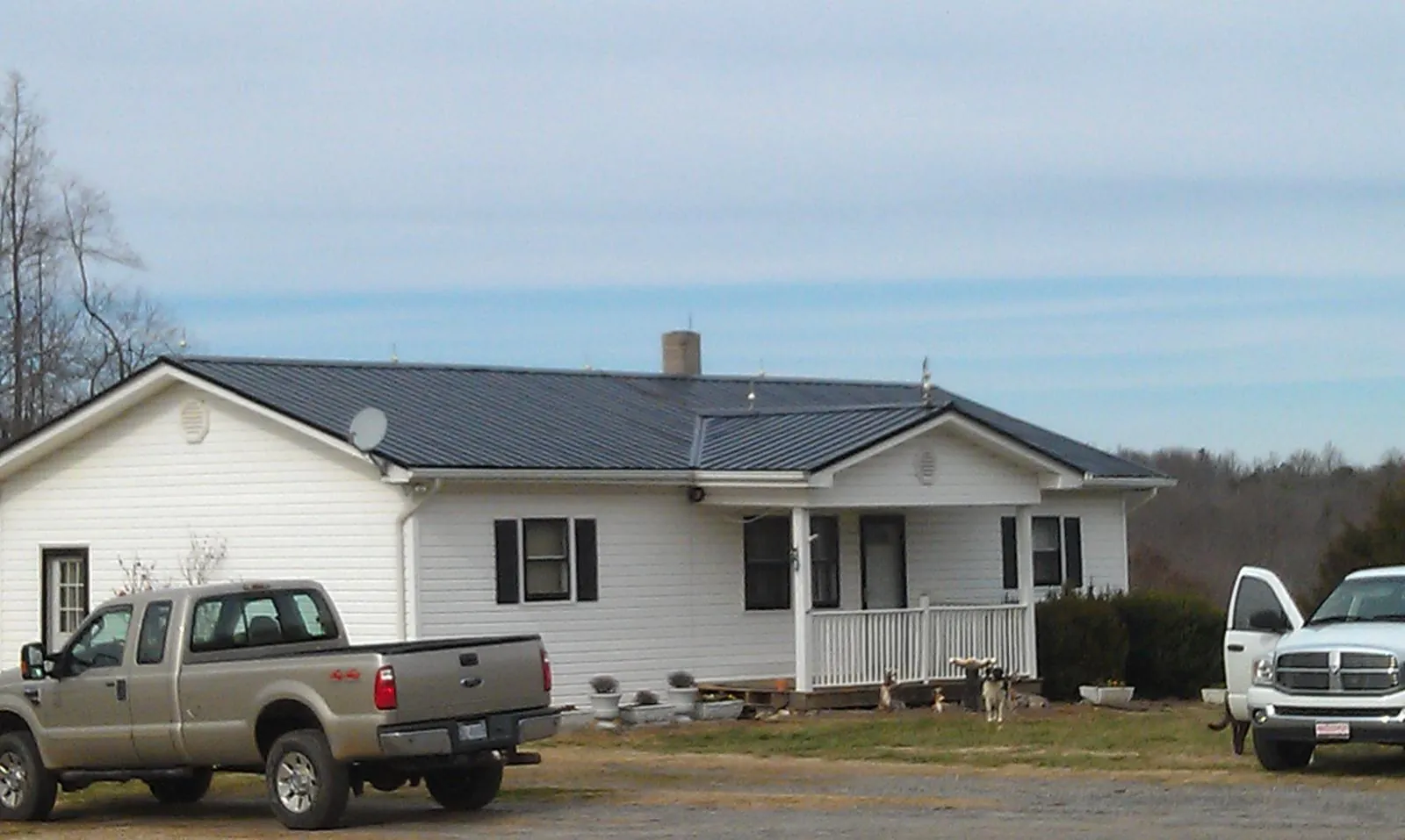 Finished dark metal roof on a white ranch home with work trucks parked in Goleta